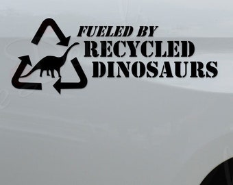 May include: A white pickup truck with a black decal on the back that says "Fueled by Recycled Dinosaurs" with a recycling symbol and a dinosaur inside.
