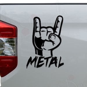 May include: Black and white decal of a hand making the rock and roll hand gesture with the word "METAL" underneath. The decal is on the back of a white pickup truck.
