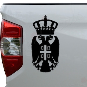 May include: Black and white decal of a double-headed eagle with a crown on top. The eagle is holding a cross with the letters '3E' on it. The decal is on the back of a white pickup truck.