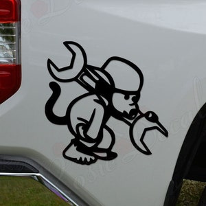 May include: Black and white decal of a cartoon mechanic holding a wrench. The decal is applied to the side of a white pickup truck.