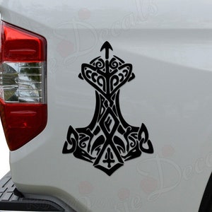 May include: Black and white tribal style Mjolnir hammer decal on a white truck tailgate.