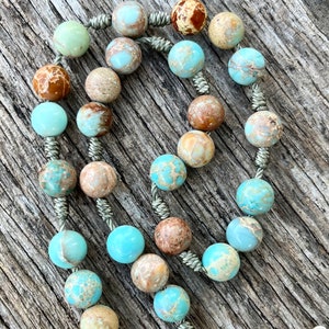 May include: A light blue and brown stone rosary with a silver cord and a silver pendant.