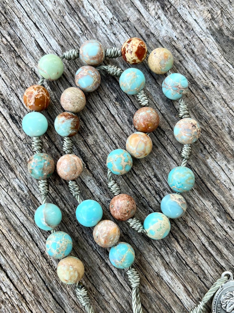 May include: A light blue and brown stone rosary with a silver cord and a silver pendant.