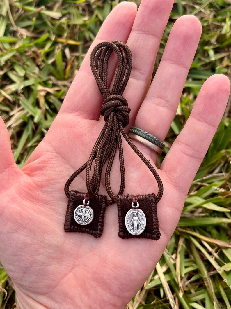 May include: Two small brown fabric pouches with silver charms hanging from brown cords. The charms are a silver oval with a woman's image and a silver cross with four smaller crosses.