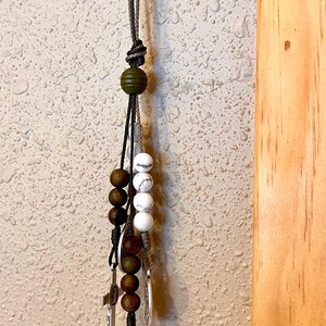 May include: A brown and white beaded keychain with a silver charm featuring a religious figure. The charm has the words "Fidelis Ad Mortem" and "Senia Vivar" inscribed around the edge.