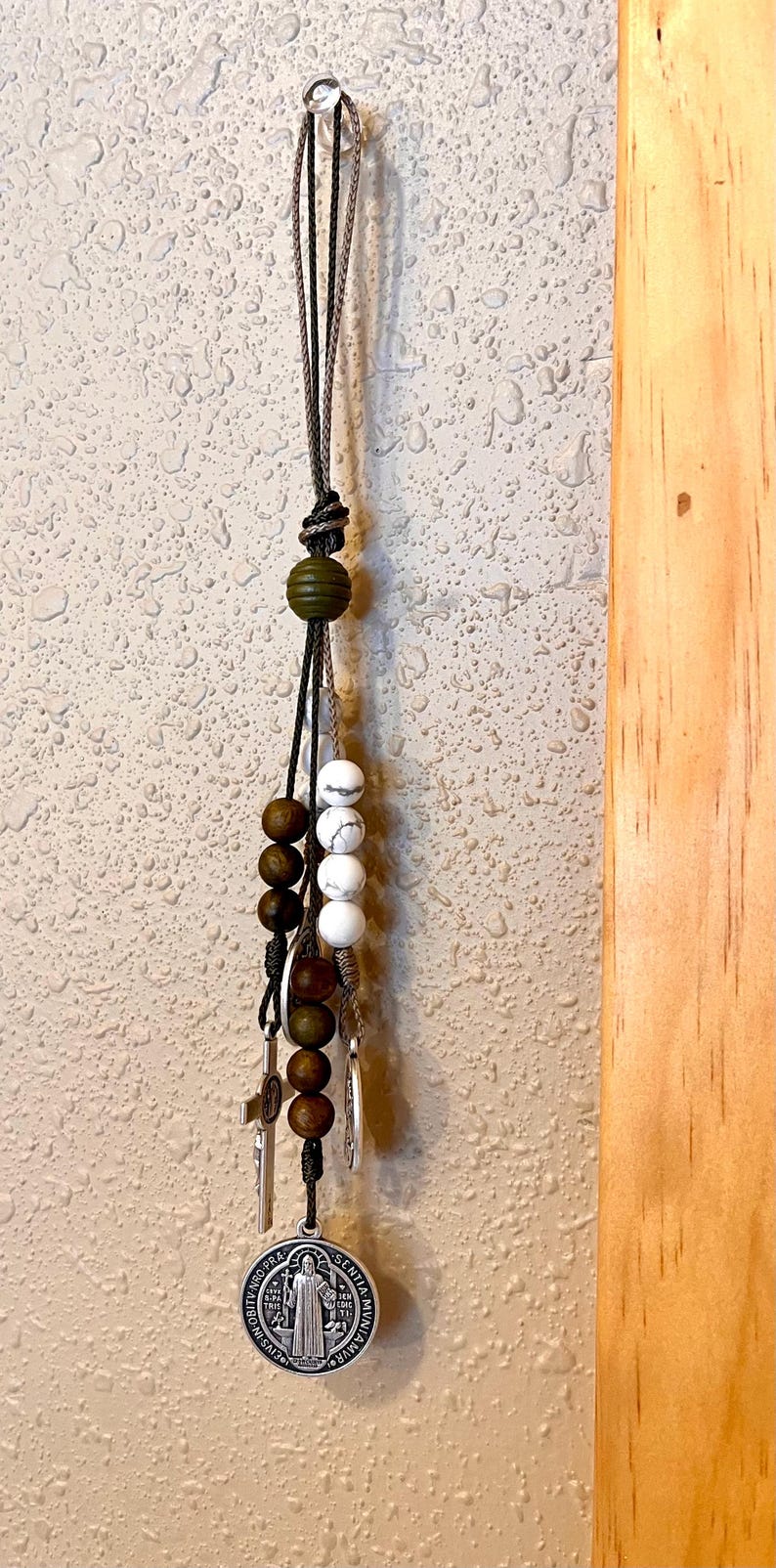 May include: A brown and white beaded keychain with a silver charm featuring a religious figure. The charm has the words "Fidelis Ad Mortem" and "Senia Vivar" inscribed around the edge.