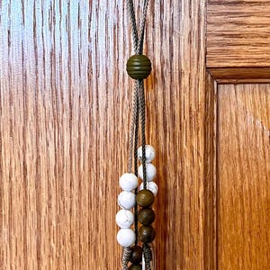May include: A silver charm bracelet with a variety of charms, including a cross, a saint medal, and a few round beads. The bracelet is hanging from a doorknob.