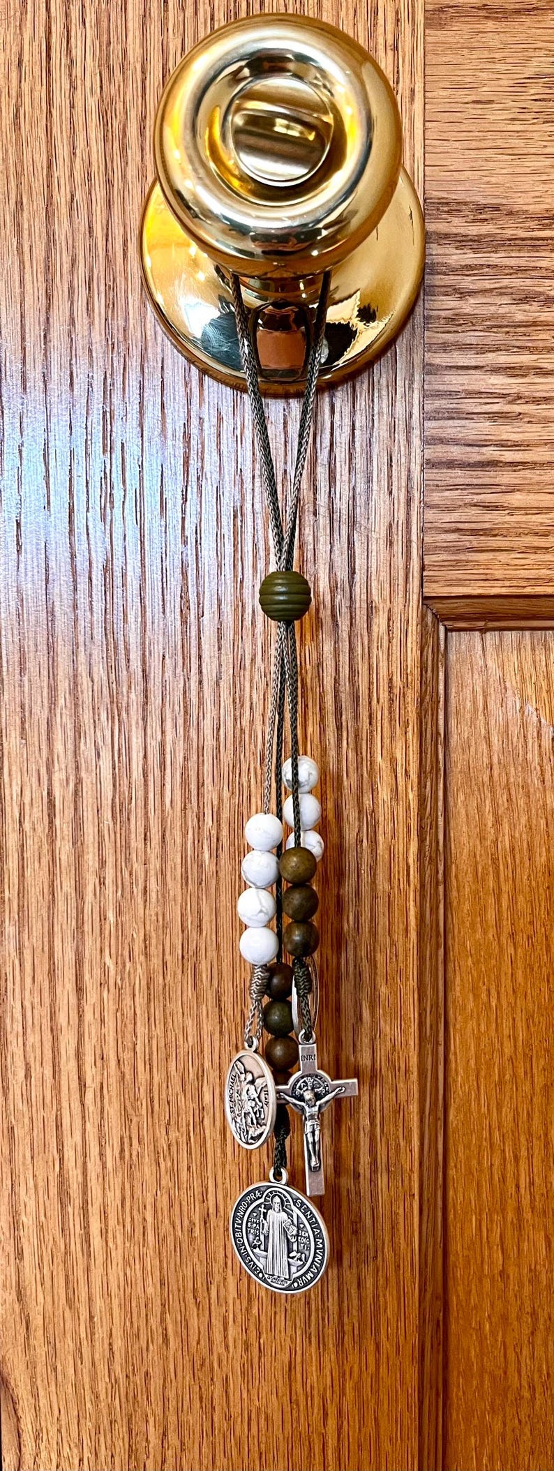 May include: A silver charm bracelet with a variety of charms, including a cross, a saint medal, and a few round beads. The bracelet is hanging from a doorknob.