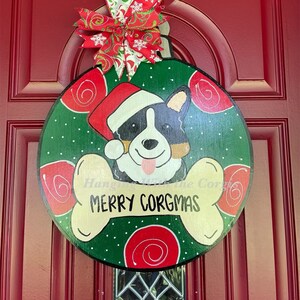 May include: A green and red Christmas ornament with a white bone shape and the text "Merry Corgmas". A cartoon Corgi dog wearing a Santa hat is in the center of the ornament.