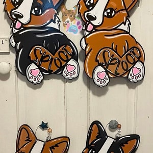 Puede incluir: Cuatro recortes de madera de corgis en diferentes poses. Dos son marrones y blancos con la palabra "SPLOOT" en la espalda. Uno es negro y blanco con la palabra "welcome" en la espalda. El &uacute;ltimo es marr&oacute;n y blanco con la palabra "welcome" en la espalda.