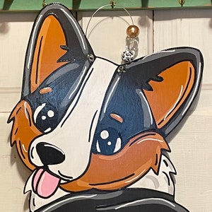 May include: A wooden cutout of a cartoon dog with black, white, and brown fur. The dog has large, round eyes and a pink tongue sticking out. The dog is wearing a black and white scarf.
