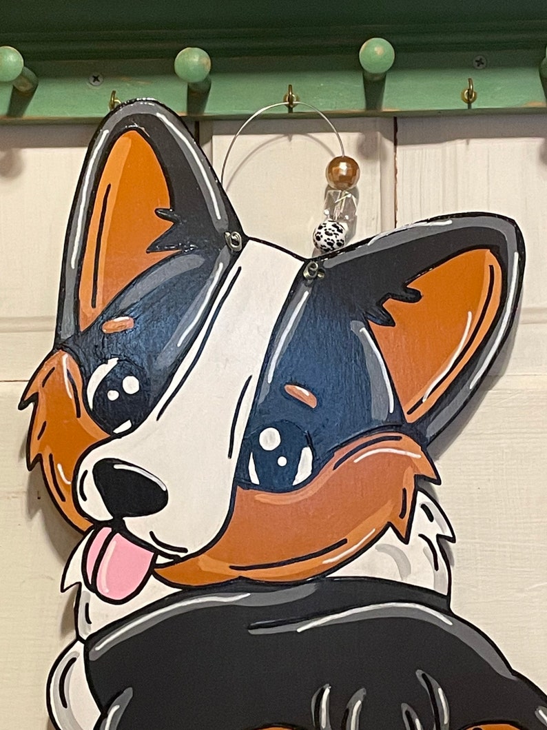 May include: A wooden cutout of a cartoon dog with black, white, and brown fur. The dog has large, round eyes and a pink tongue sticking out. The dog is wearing a black and white scarf.