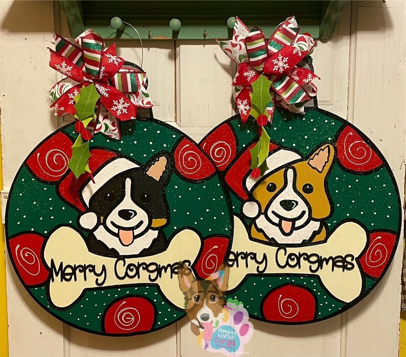 May include: Two Christmas ornaments featuring a black and white and a brown and white corgi dog wearing Santa hats. The ornaments are green with red and white swirls and the text "Merry Corgmas" on a bone.