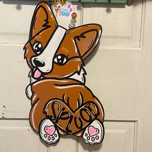 May include: A brown and white cartoon dog with a pink heart and the word "SPLOOT" on its back. The dog has pink hearts on its paws and is painted on a wooden surface.