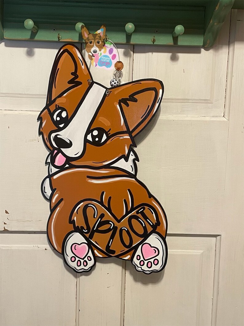 May include: A brown and white cartoon dog with a pink heart and the word "SPLOOT" on its back. The dog has pink hearts on its paws and is painted on a wooden surface.