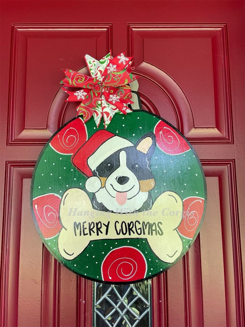 May include: A green and red Christmas ornament with a white bone shape and the text "Merry Corgmas". A cartoon Corgi dog wearing a Santa hat is in the center of the ornament.