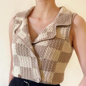 Può includere: Un gilet all'uncinetto con scollo a camicia e un motivo a scacchi beige e bianco.