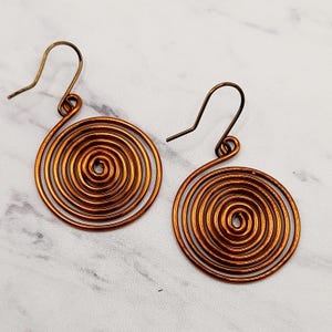 May include: A pair of copper wire earrings with a spiral design. The earrings are a light copper colour and have a simple hook fastening.