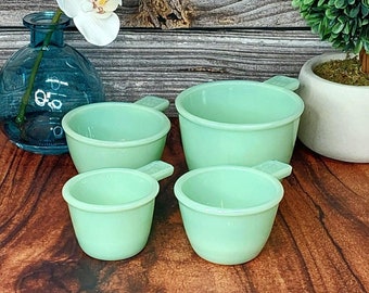 May include: Set of four vintage green measuring cups with handles. The cups are made of glass and have a frosted finish.