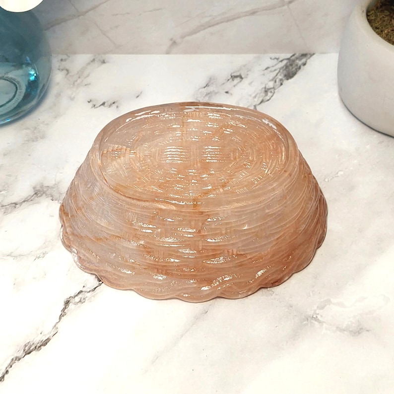 May include: A small, light brown, basket-weave textured bowl. The bowl has a rounded shape with a scalloped edge. The bowl is made of a translucent material, and the weave pattern is visible throughout the bowl.