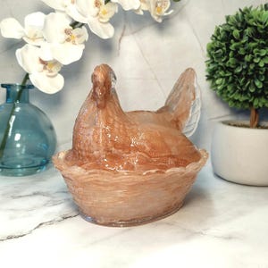 May include: A decorative, translucent hen figurine in a nest-like bowl. The hen is a light brown color with a textured surface. The bowl has a wavy rim. The figurine is a unique home decor item.