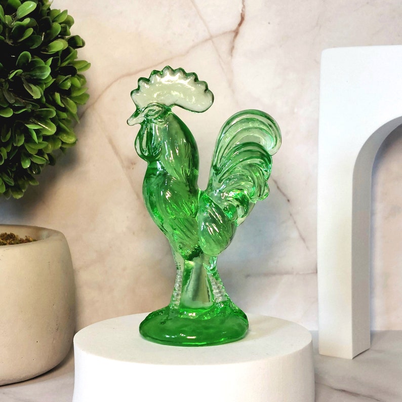May include: A green glass rooster figurine with a detailed design. The rooster has a white crest and a long tail.