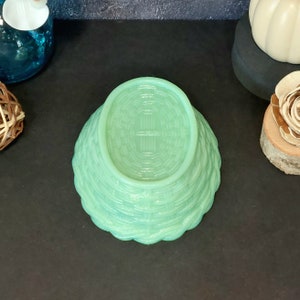 May include: A light green, basket-weave patterned bowl. The bowl is upside down, revealing the woven texture on the bottom. The bowl's edges have a scalloped design. The bowl is made of glass or a similar material.