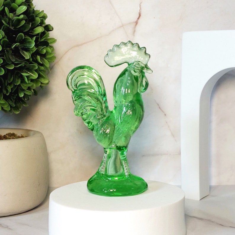 May include: A green glass rooster figurine with a white crest. The rooster is standing on a round base.
