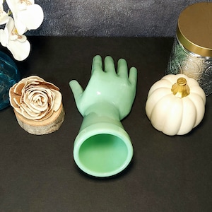 May include: A light green glass hand-shaped vase with a smooth, glossy finish. The vase is empty and ready to hold flowers.