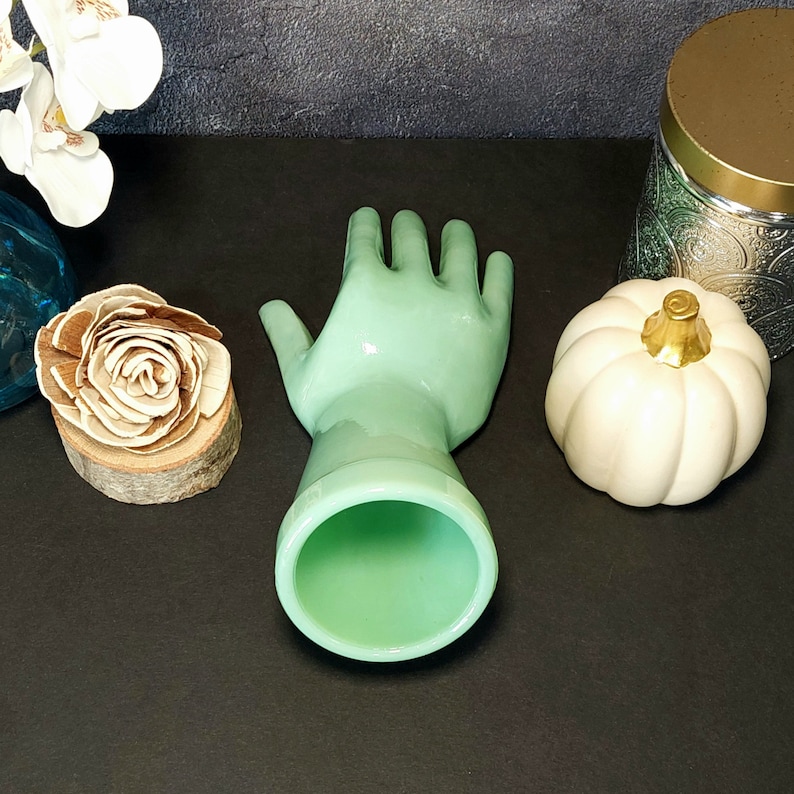 May include: A light green glass hand-shaped vase with a smooth, glossy finish. The vase is empty and ready to hold flowers.