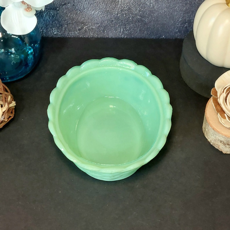 May include: A light green, scalloped-edge bowl. The bowl has a textured exterior and a smooth interior. The bowl is empty and sits on a dark surface. The bowl is likely made of glass or ceramic.
