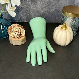 May include: A light green rubber glove with five fingers. The glove is on a dark gray surface.