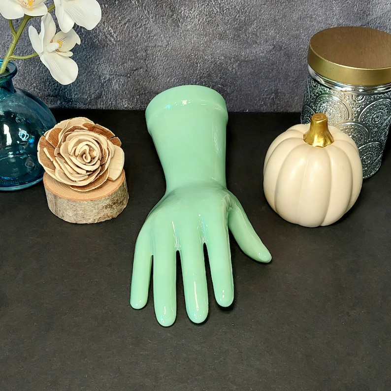 May include: A light green rubber glove with five fingers. The glove is on a dark gray surface.
