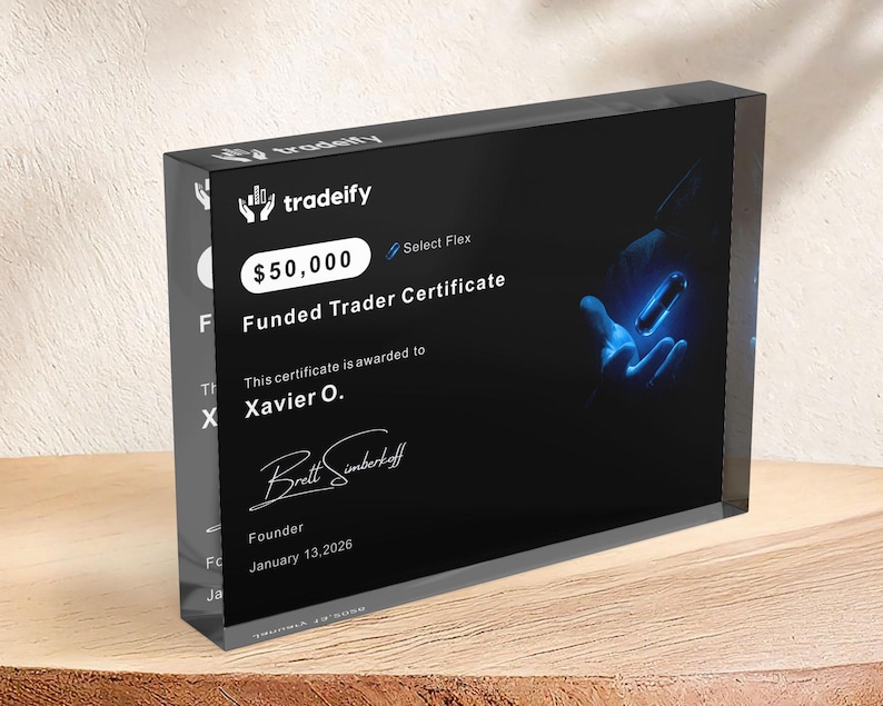 Puede incluir: Un bloque rectangular de acr&iacute;lico negro que muestra un certificado de trader financiado de Tradeify por $50,000. El certificado presenta el nombre Xavier O., una firma del fundador Brett Simberkoff, la fecha 13 de enero de 2026 y un gr&aacute;fico azul brillante.