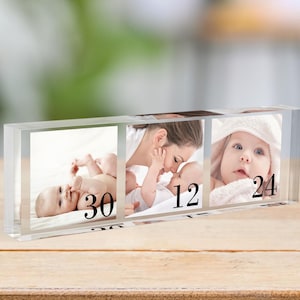 Op de afbeelding: Een transparante acrylblokken fotolijst met drie aparte fotogleuven. De lijst toont drie foto's van een baby op verschillende leeftijden, met de nummers 30, 12 en 24 onder elke foto.