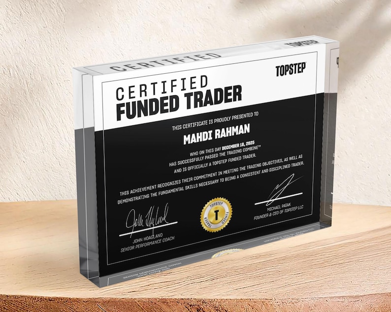 Puede incluir: Un bloque rectangular de acr&iacute;lico transparente con un certificado en blanco y negro de Certified Funded Trader. El texto dice Topstep, Certified Funded Trader, Mahdi Rahman, 18 de diciembre de 2025, e incluye firmas y un sello dorado.
