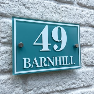 Puede incluir: Un letrero rectangular turquesa con el número "49" y el nombre "BARNHILL" en letras blancas. Fijado a una pared de ladrillos blancos con dos tornillos plateados.