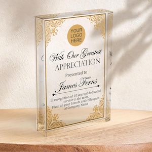 May include: A gold and white glass plaque with an ornate border and a black inscription. The inscription reads "With Our Greatest Appreciation" and "Presented to James Ferns". The text continues with "In recognition of 10 years of dedicated service to the team. From all your friends and colleagues at Company Name."