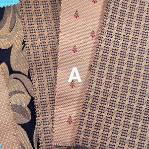 May include: A collection of five fabric swatches in various patterns and colours. The swatches are arranged vertically, with the letter "A" written in white on the fourth swatch. The swatches are all brown, beige, and black.
