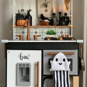 May include: A black and white play kitchen with a copper tap, a ghost tea towel, and a sign that says "boo" with a spider's web and spider.