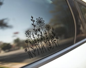 Könnte beinhalten: Ein schwarzer Vinyl-Aufkleber auf einer Autoscheibe, der eine Strichzeichnung eines Bündels von Wildblumen zeigt, einschließlich Gänseblümchen, Stängeln und Blättern, die in einer vertikalen, organischen Komposition angeordnet sind.