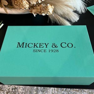 May include: A turquoise blue box with the text "MICKEY & CO. SINCE 1928" printed in black.
