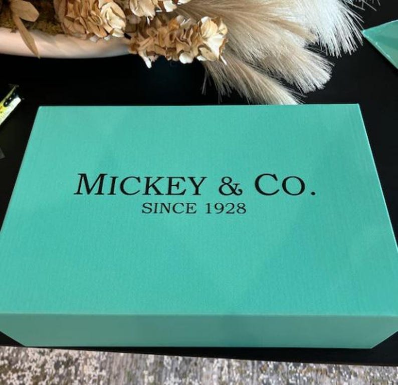 May include: A turquoise blue box with the text "MICKEY & CO. SINCE 1928" printed in black.