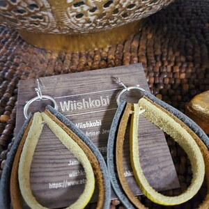 May include: A pair of leather earrings with a teardrop shape. The earrings are made of three layers of leather in brown, yellow, and gray. The earrings are attached to silver hooks.
