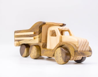 May include: A wooden toy dump truck with a brown and natural wood finish. The truck has four wheels and a raised bed.