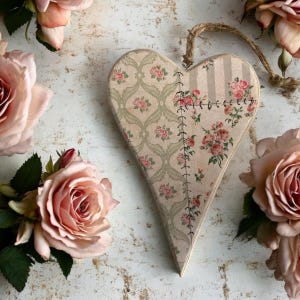May include: A heart-shaped wooden ornament with a patchwork design featuring floral patterns in shades of pink and green. The ornament is decorated with stitched seams and has a rustic, vintage aesthetic.