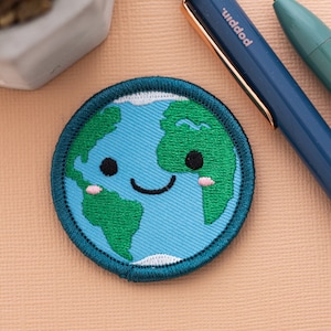 An iron-on patch of the Earth with a cute smiling face and small pink cheeks