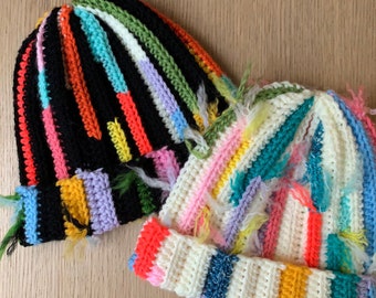 May include: Two colorful crocheted hats with a striped pattern. One hat is black with multi-colored stripes and the other is white with multi-colored stripes.