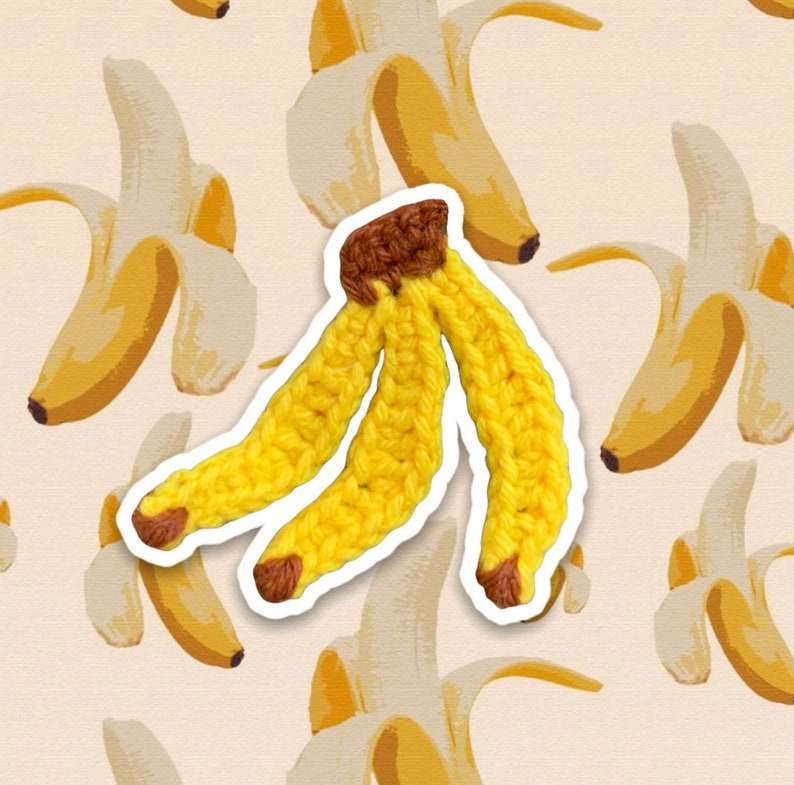 Puede incluir: Un pl&aacute;tano de crochet con una punta marr&oacute;n. El pl&aacute;tano est&aacute; hecho de hilo amarillo y tiene una forma tridimensional.