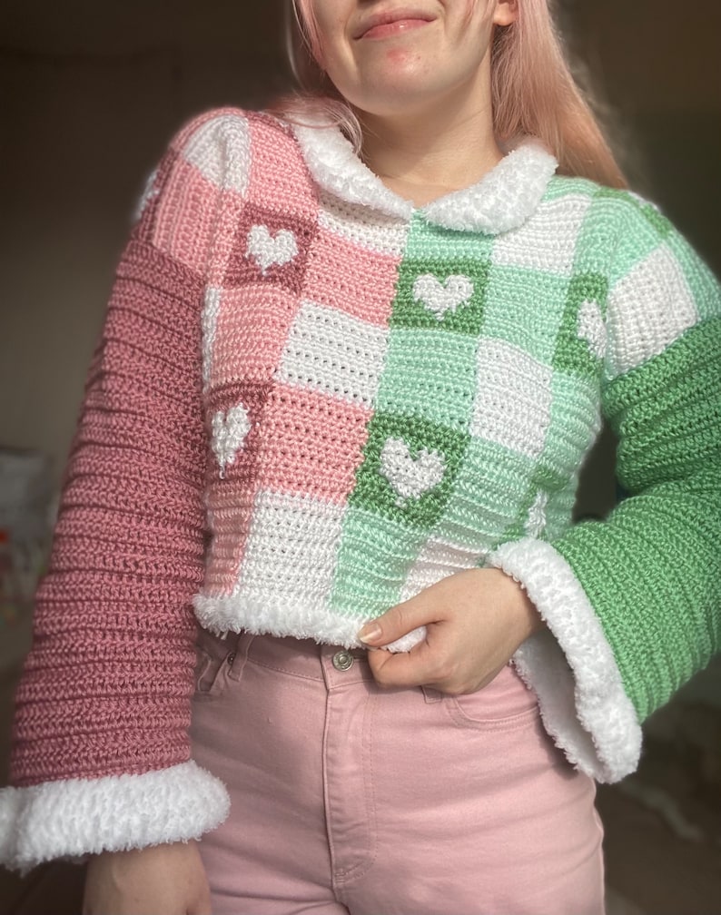 Pu&ograve; includere: Un maglione all'uncinetto rosa e verde con cuori bianchi e un colletto all'uncinetto bianco.